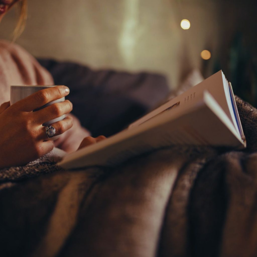 woman reading a book while bundled up with a blanket.